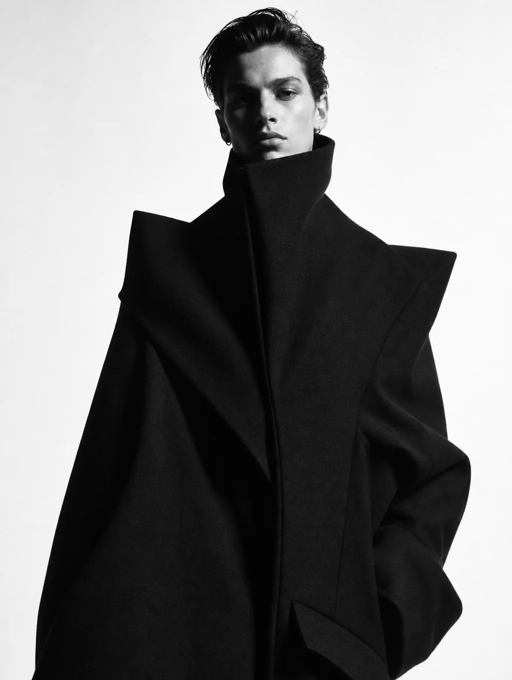 Model wearing an ARVÉ heavy-drape coat against an obsidian monolithic backdrop